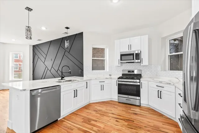 a kitchen with stainless steel appliances granite countertop a stove top oven a sink dishwasher and a refrigerator with wooden floor