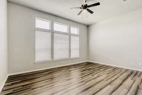 an empty room with wooden floor fan and windows