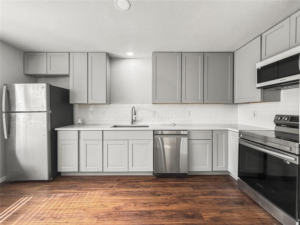 5840 Spring Valley Road, Unit 1104 Dallas, TX 75254 - Photo 12 of 16 Modern kitchen featuring light gray shaker-style cabinetry, a white subway tile backsplash, and wood-finish flooring