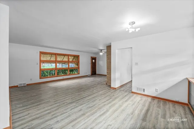 an empty room with wooden floor chandelier and windows