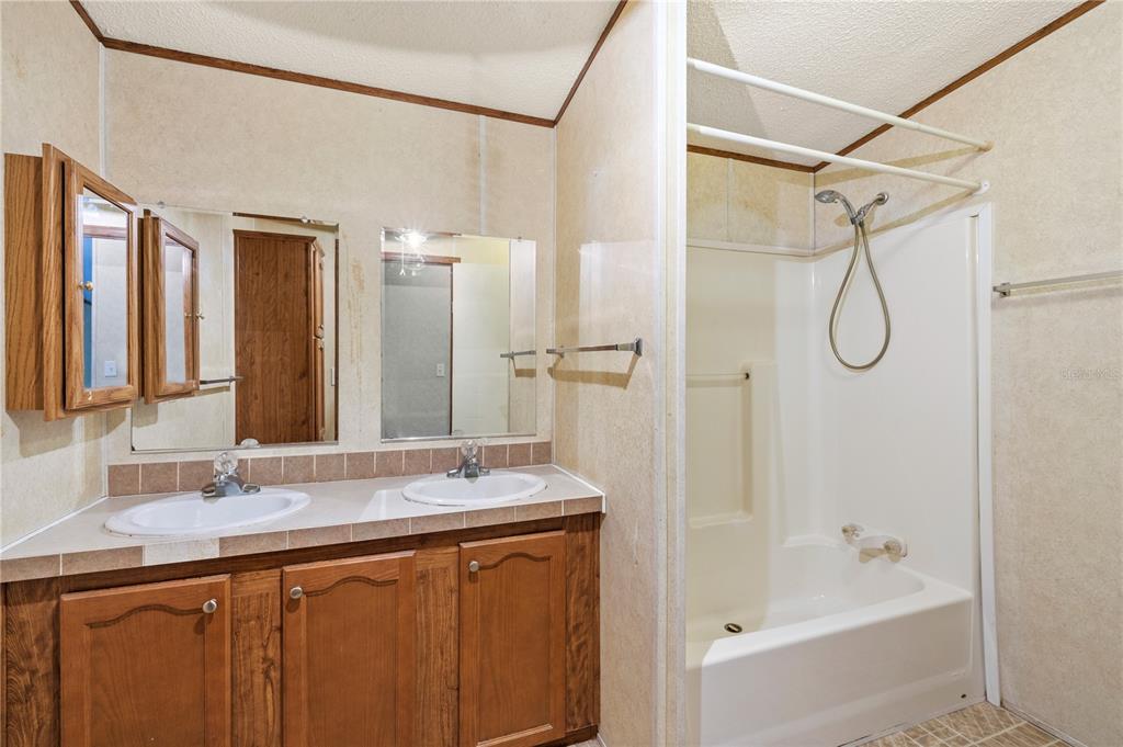 32443 Memory Lane Leesburg, FL 34788 - Photo 37 of 51 a bathroom with a granite countertop sink a mirror a bathtub and shower
