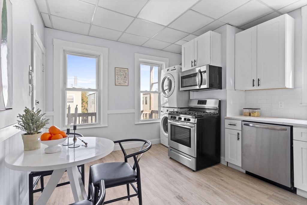 742 Bennington Street, Unit 3 Boston, MA 02128 - Photo 8 of 16 a kitchen with stainless steel appliances a stove a sink dishwasher a microwave oven and a dining table with wooden cabinet