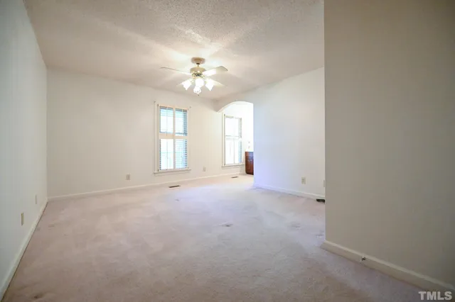 an empty room with chandelier fan and windows