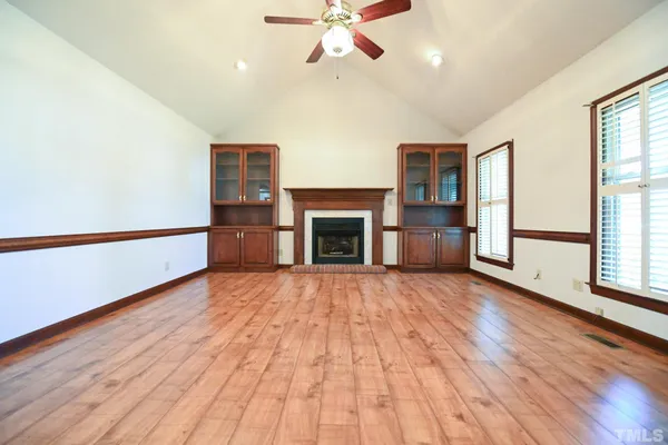 an empty room with wooden floor fireplace and windows