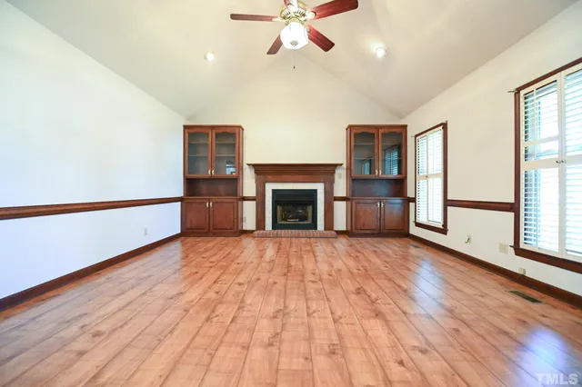 an empty room with wooden floor fireplace and windows