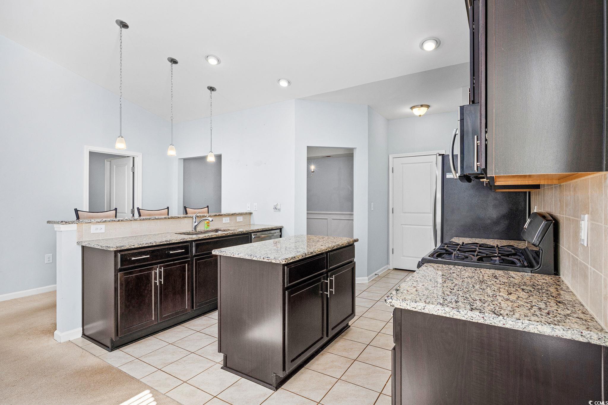 817 Arezzo Way, Unit 1001 Myrtle Beach, SC 29579 - Photo 17 of 40 Kitchen featuring dark brown cabinetry, a center island, light stone counters, hanging light fixtures, and stainless steel appliances