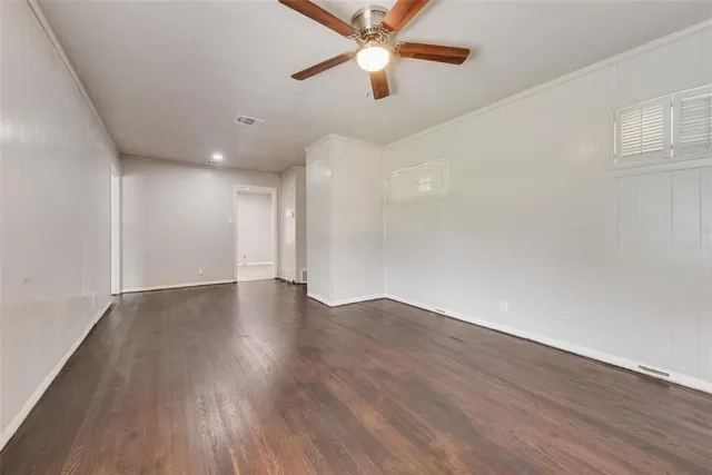 a view of an empty room with wooden floor and a ceiling fan