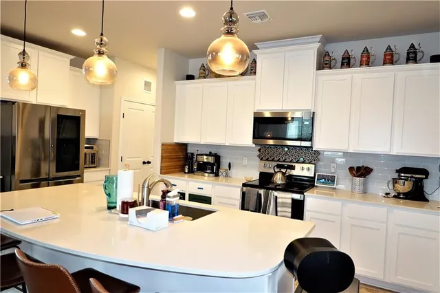 a kitchen with stainless steel appliances a stove a refrigerator a sink a dining table and chairs with wooden floor