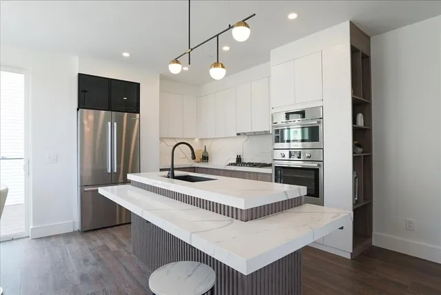 a kitchen with stainless steel appliances granite countertop a sink a stove a refrigerator and island with wooden floor