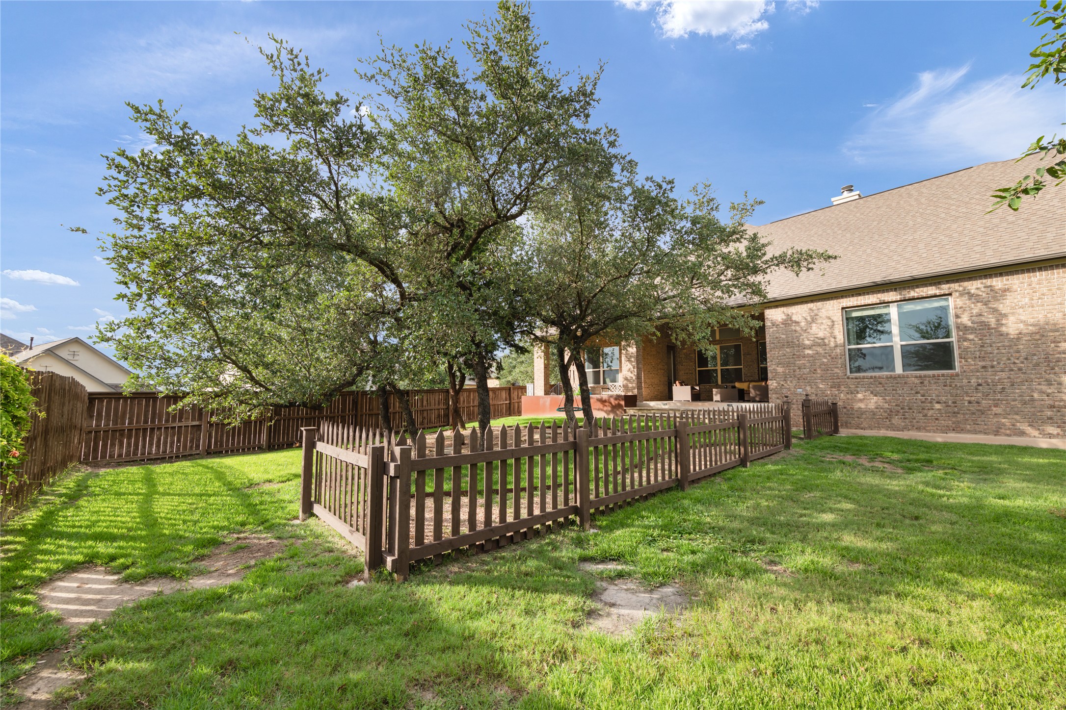 415 Bitterroot Lane Austin, TX 78737 - Photo 23 of 25 Mature trees shade a private backyard, featuring a charming picket fence and brick exterior.
