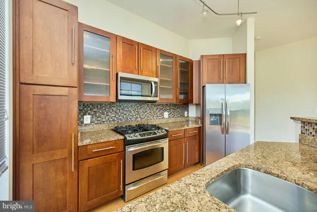 a kitchen with stainless steel appliances granite countertop a refrigerator a stove and a sink with wooden cabinets