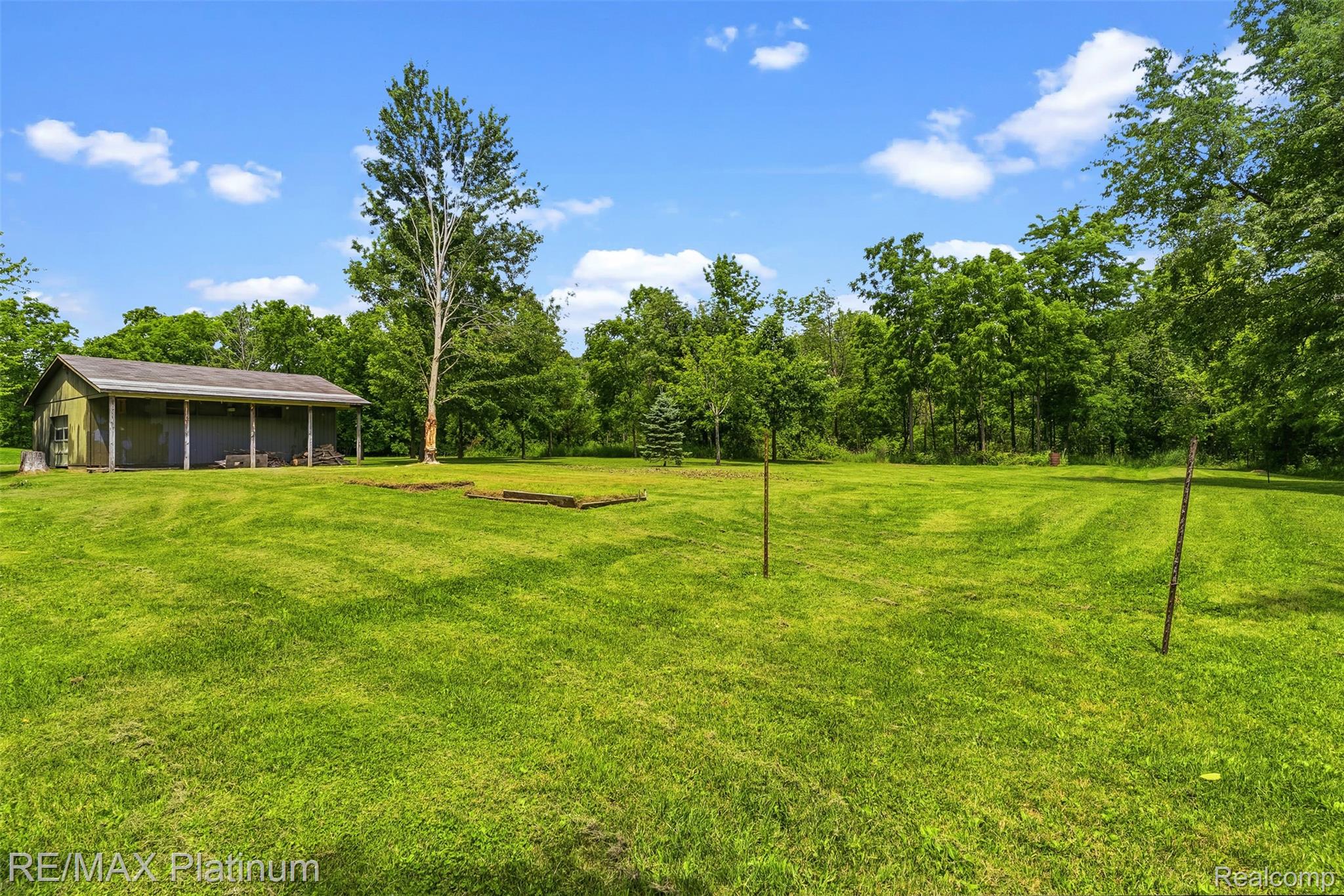 8370 West Rolston Road Linden, MI 48451 - Photo 32 of 36 Expansive green space featuring a large outbuilding with a covered porch, mature trees, and a clear blue sky