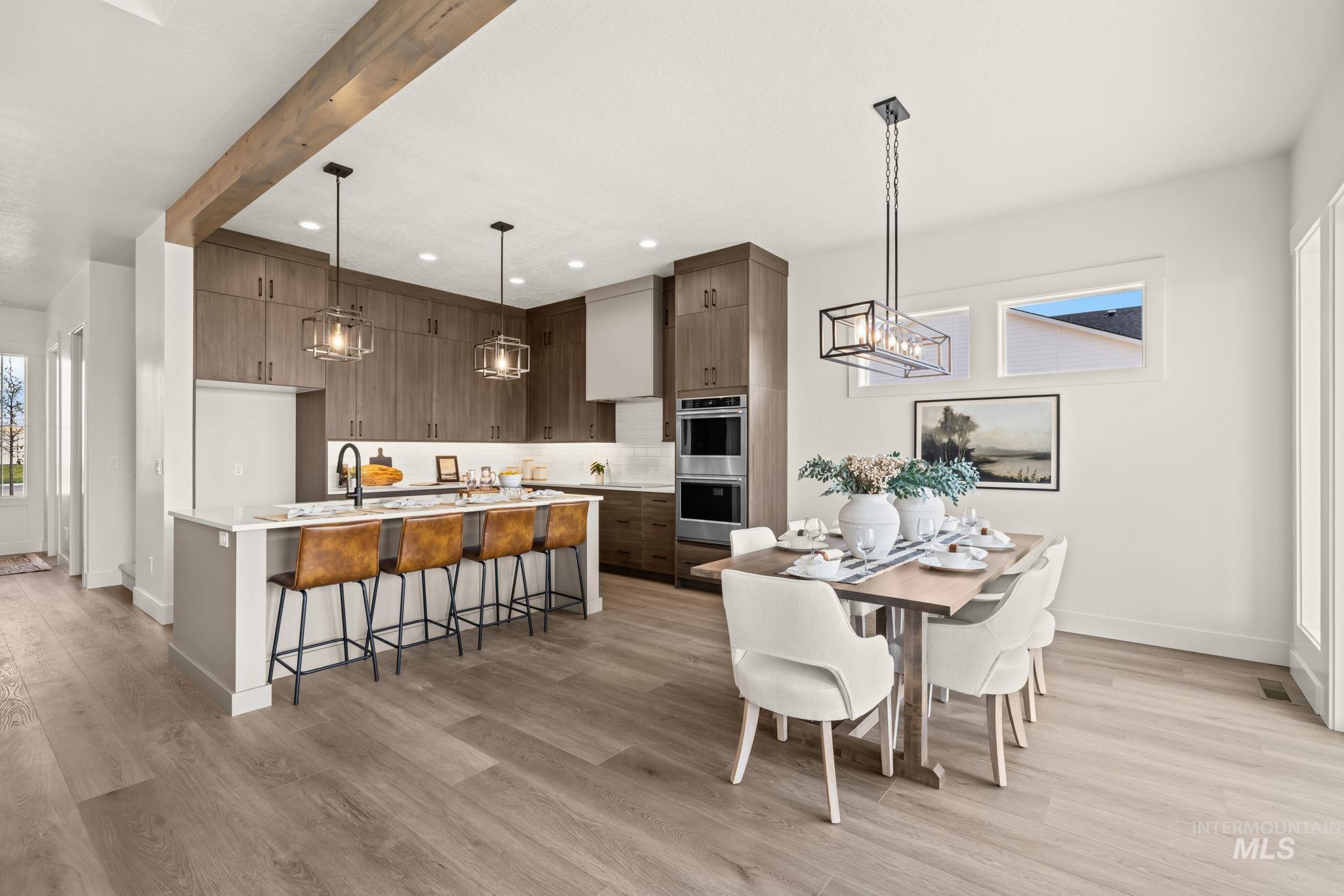 345 South Strut Way Boise, ID 83716 - Photo 14 of 50 Kitchen and dining area featuring wood-finish flooring, a kitchen island with seating, dark wood-finish cabinetry, a built-in double oven, and a linear chandelier