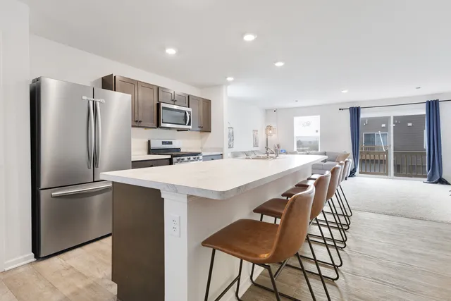 a kitchen with stainless steel appliances granite countertop a refrigerator a sink a stove a dining table and chairs