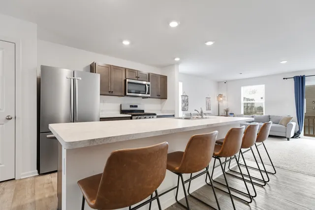 a kitchen with stainless steel appliances granite countertop a dining table chairs refrigerator and cabinets