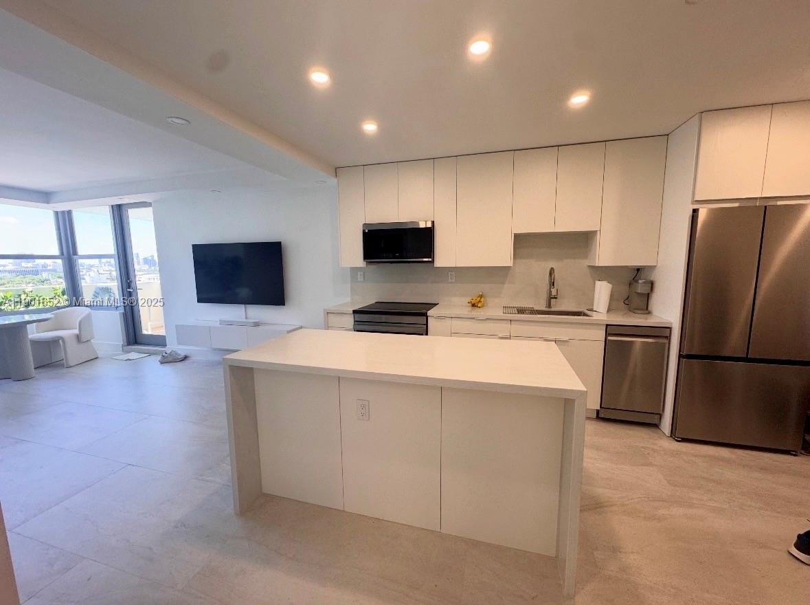2899 Collins Avenue, Unit 1414 Miami Beach, FL 33140 - Photo 3 of 26 a kitchen with a refrigerator a stove top oven a sink dishwasher and white cabinets with wooden floor