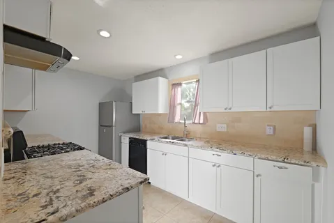 a kitchen with granite countertop a sink stainless steel appliances white cabinets and a window