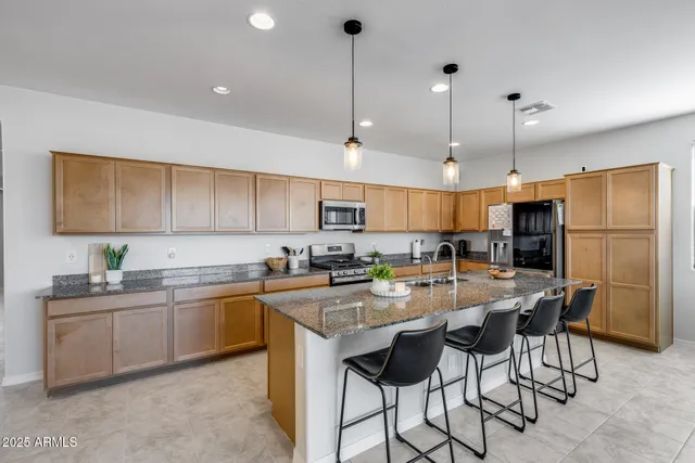 a kitchen with stainless steel appliances granite countertop a sink a stove a refrigerator cabinets and chairs