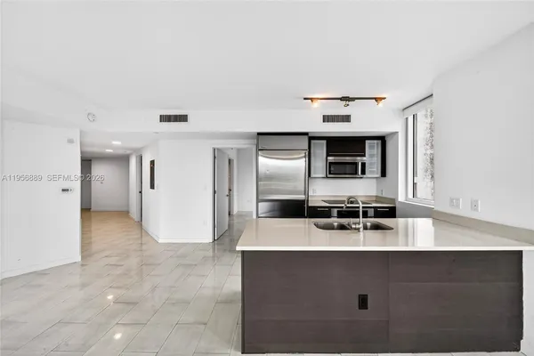 a view of an empty room with kitchen and window