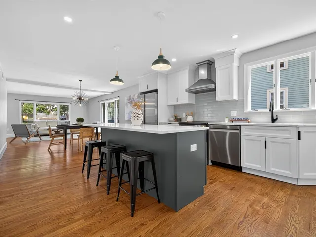 a kitchen with stainless steel appliances granite countertop a stove a sink dishwasher a microwave oven and a dining table with wooden floor