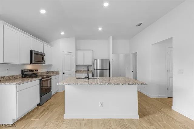 a large kitchen with stainless steel appliances granite countertop a stove a sink a refrigerator and white cabinets with wooden floor