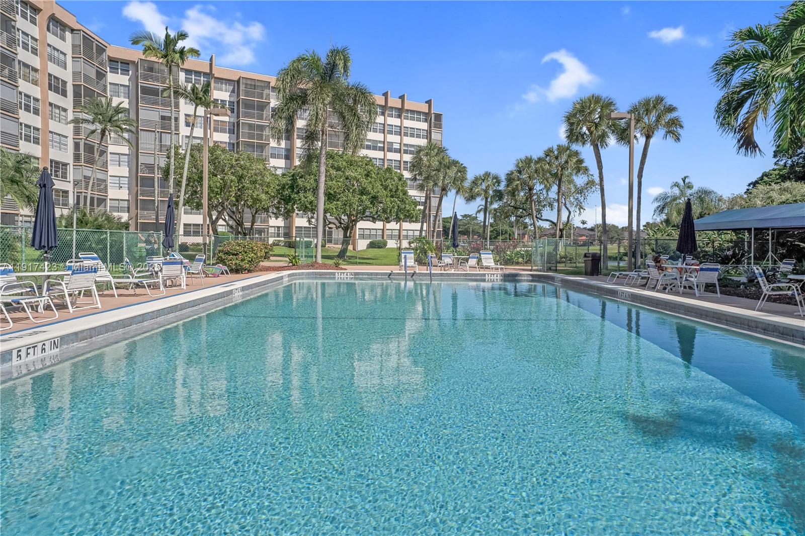 1200 St Charles Place, Unit 716 Pembroke Pines, FL 33026 - Photo 24 of 29 a swimming pool that has lawn chairs and a dining table under an umbrella