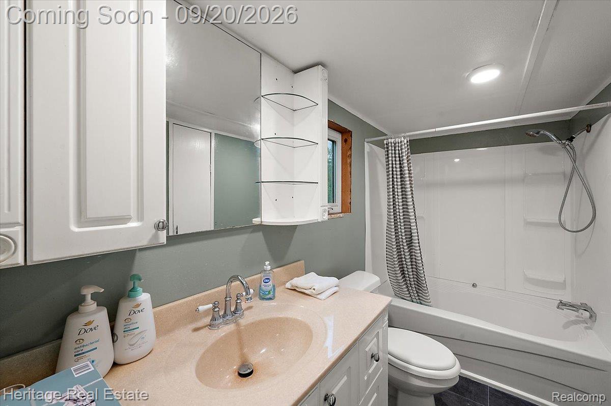 3337 Le Valley Road Columbiaville, MI 48421 - Photo 17 of 57 Bathroom featuring a single vanity with an integrated sink, wall-mounted mirrored cabinetry, corner shelving, and a full bathtub with shower