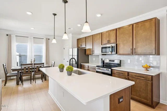 a kitchen with stainless steel appliances a stove a sink a oven a dining table with white cabinets and wooden floor