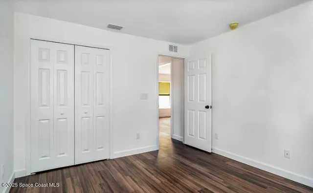 a view of an empty room with wooden floor and closet area