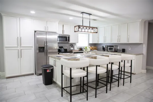 a kitchen with stainless steel appliances kitchen island granite countertop a refrigerator a sink a stove a dining table and chairs