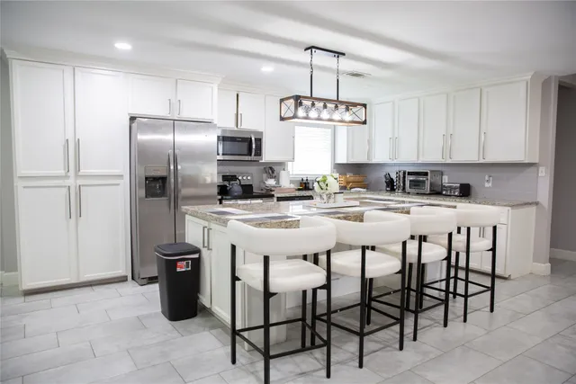 a kitchen with stainless steel appliances kitchen island granite countertop a refrigerator a sink a stove a dining table and chairs