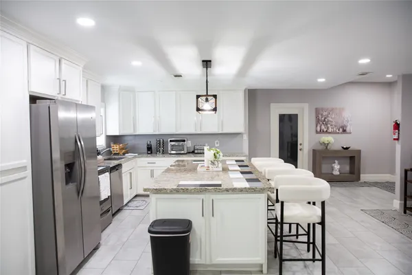 a kitchen with stainless steel appliances granite countertop a sink a stove a dining table with chairs and white cabinets