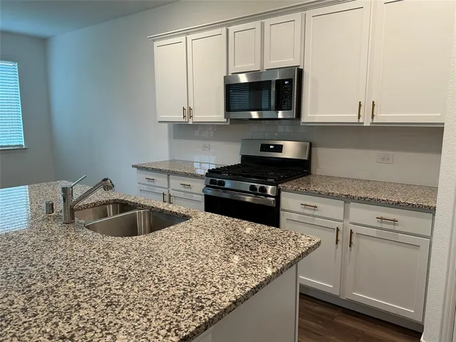 a kitchen with granite countertop a sink a stove a microwave and cabinets