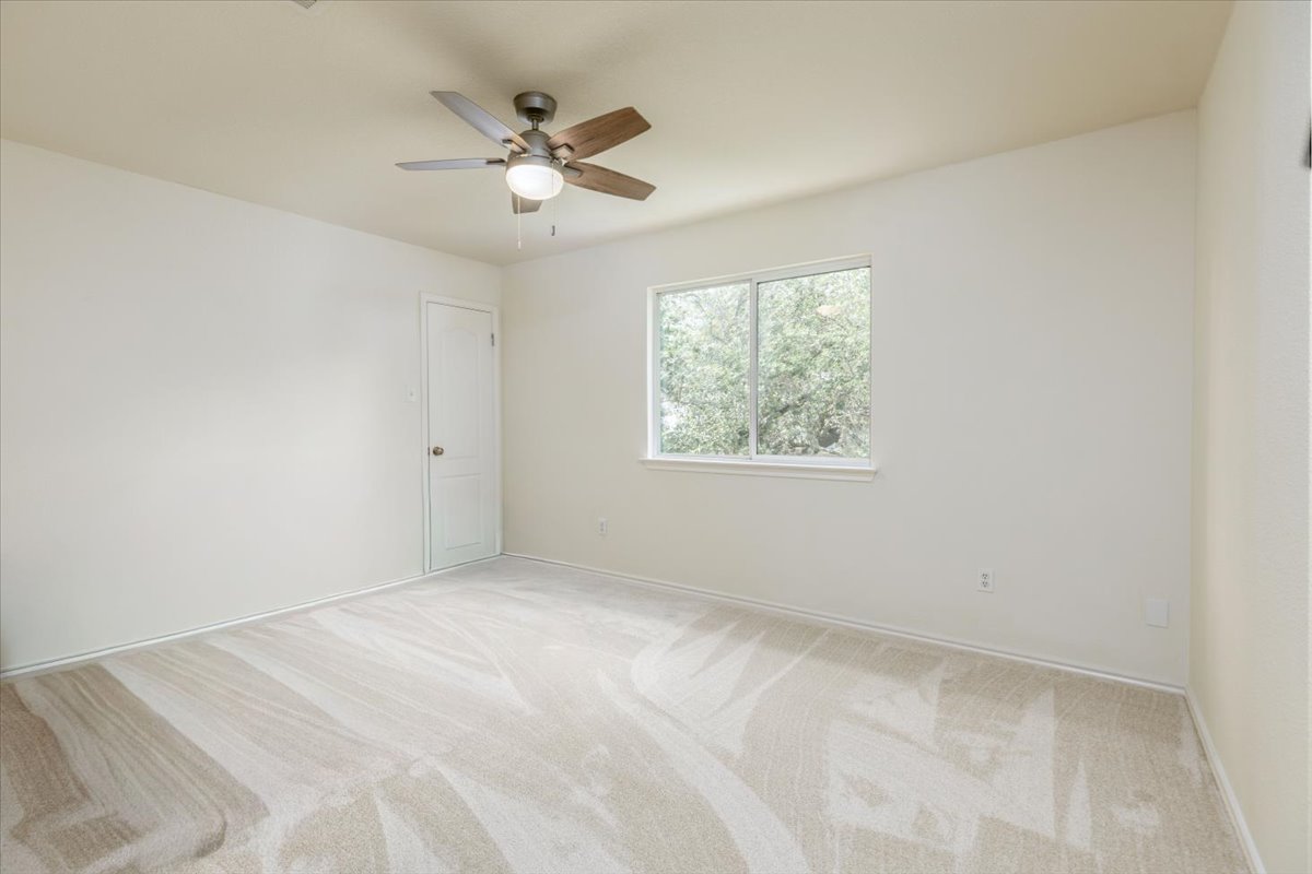 7136 Ridge Oak Road Austin, TX 78749 - Photo 15 of 28 A well-proportioned bedroom offers fresh carpet, a ceiling fan, and a serene window view of leafy trees.