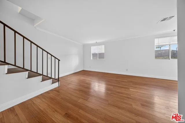 a view of an empty room with wooden floor and fan