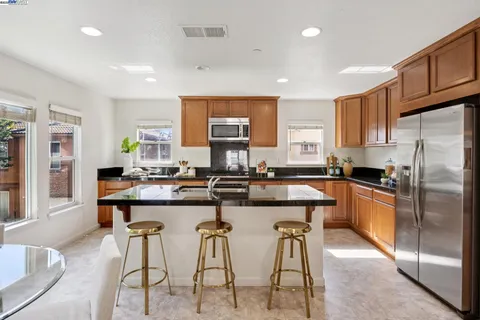 a kitchen with stainless steel appliances granite countertop a stove a sink a refrigerator cabinets and a dining table
