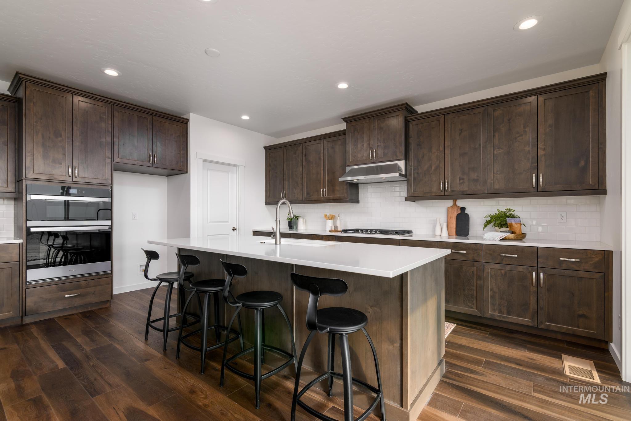 1922 West Declan Street Kuna, ID 83634 - Photo 4 of 9 Kitchen with dark wood finish cabinetry, a breakfast bar area, dark wood-type flooring, an island with sink, and recessed lighting