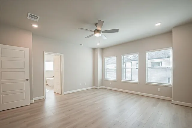 an empty room with wooden floor ceiling fan and windows