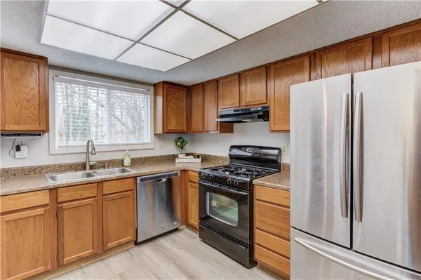 a kitchen with stainless steel appliances granite countertop white cabinets a sink a stove a refrigerator and dishwasher with wooden floor