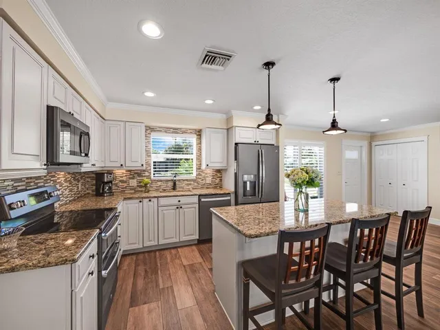 a kitchen with granite countertop kitchen island stainless steel appliances a dining table chairs sink and stove top oven