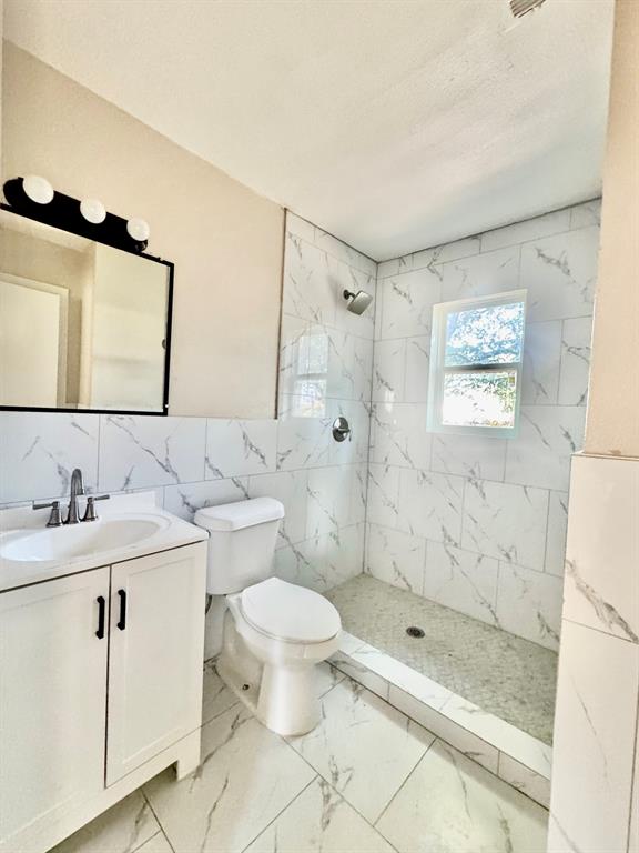 Bathroom featuring a walk-in shower with tile surround, a single vanity with a rectangular sink, and a framed mirror with overhead lighting