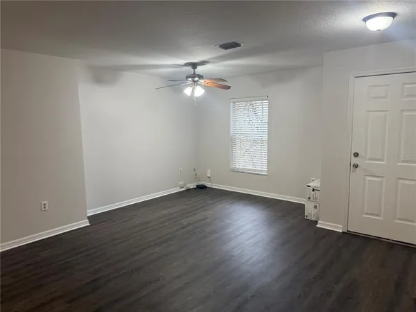 an empty room with wooden floor chandelier fan and windows