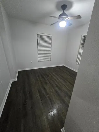 a view of an empty room with chandelier fan and wooden floor