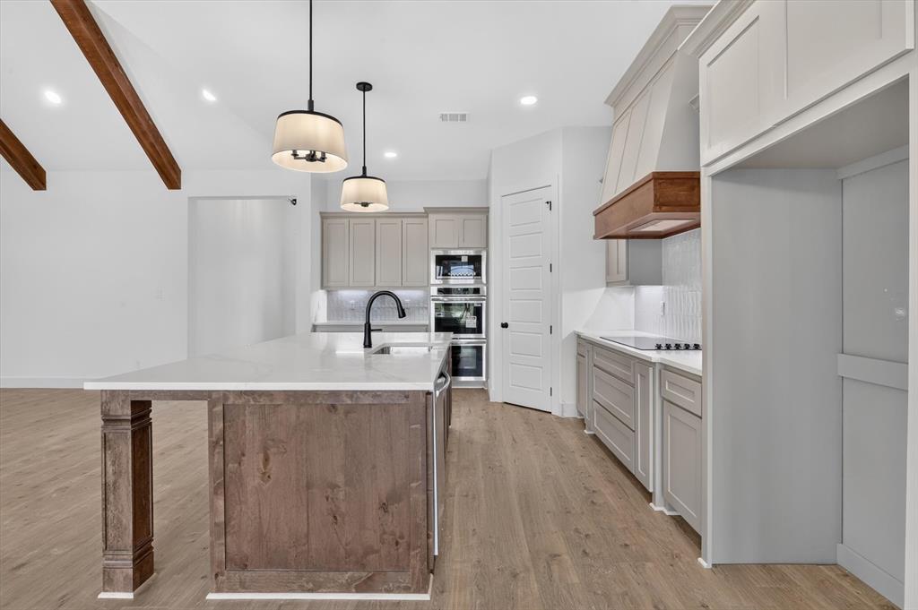 471 Red Bird Drive Springtown, TX 76082 - Photo 12 of 35 Kitchen featuring a large island with a white countertop and dark wood-finish cabinetry, light grey perimeter cabinetry, and built-in double ovens