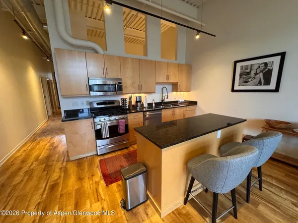 a kitchen with stainless steel appliances granite countertop a stove a refrigerator a sink a dining table and chairs with wooden floor
