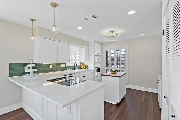 a kitchen that has a sink a microwave oven a stove and white cabinets with wooden floor