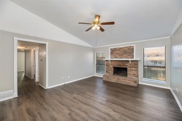 a view of an empty room with wooden floor fireplace and a window