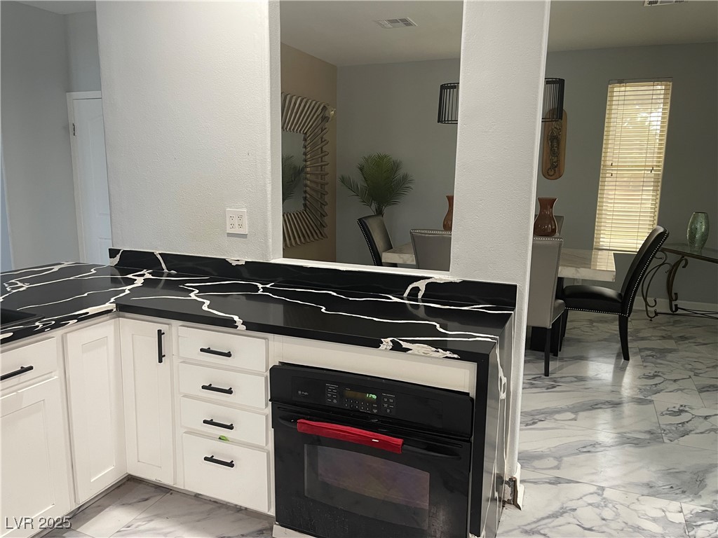 6480 West Oquendo Road Las Vegas, NV 89118 - Photo 16 of 51 Kitchen featuring light marble finish floors, oven, white cabinetry, and a peninsula