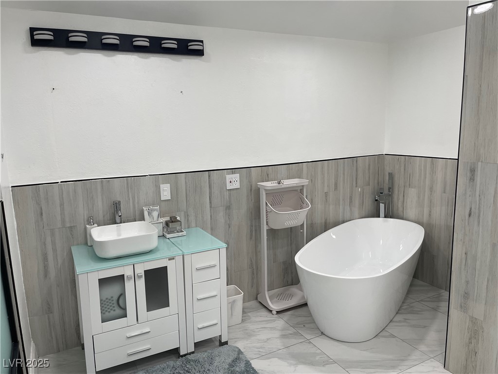 6480 West Oquendo Road Las Vegas, NV 89118 - Photo 41 of 51 Full bathroom with vanity, a freestanding tub, light marble finish floors, wainscoting, and tile walls