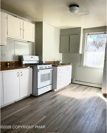 a kitchen with stainless steel appliances granite countertop a stove a sink and white cabinets with wooden floor